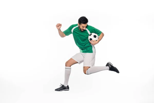 Junger Fußballer in Uniform springt mit Fußball auf weißem Grund — Stockfoto