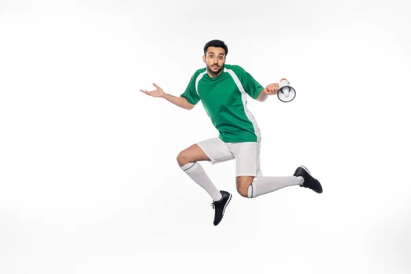 Futbolista confuso en uniforme saltando y sosteniendo el altavoz en blanco - foto de stock