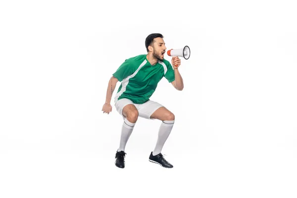 Joven futbolista en uniforme saltando y gritando en altavoz aislado en blanco - foto de stock