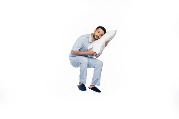 Homme barbu en pyjama lévitant avec oreiller sur blanc — Photo de stock