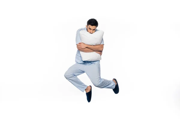 Joven en pijama levitando y abrazando almohada aislado en blanco - foto de stock