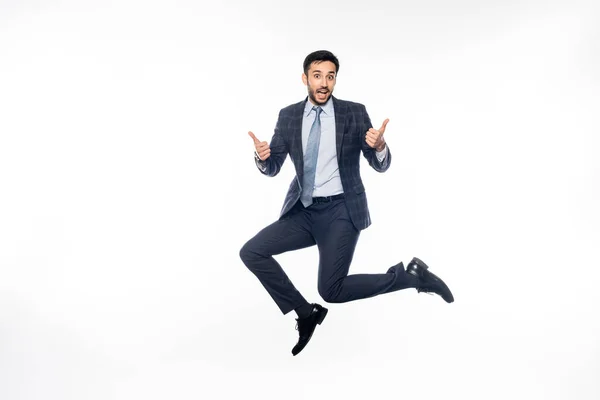 Sorprendido hombre de negocios en traje saltando mientras muestra los pulgares hacia arriba en blanco - foto de stock