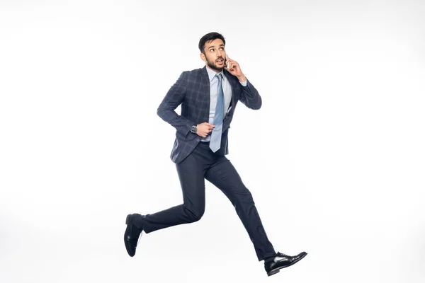 Hombre de negocios pensativo en traje saltando y hablando en el teléfono inteligente en blanco - foto de stock