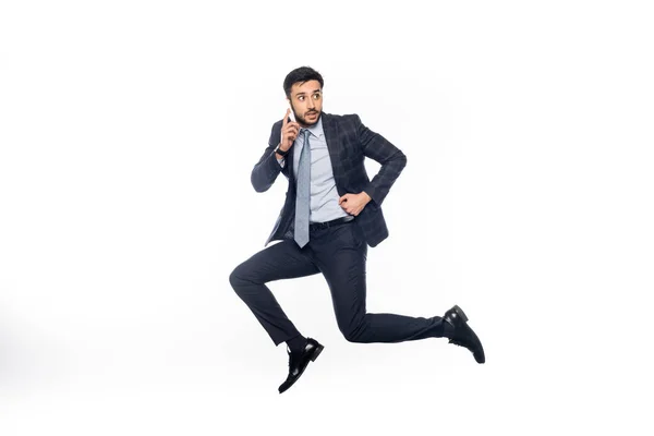 Hombre de negocios en traje saltando y hablando en el teléfono inteligente aislado en blanco - foto de stock