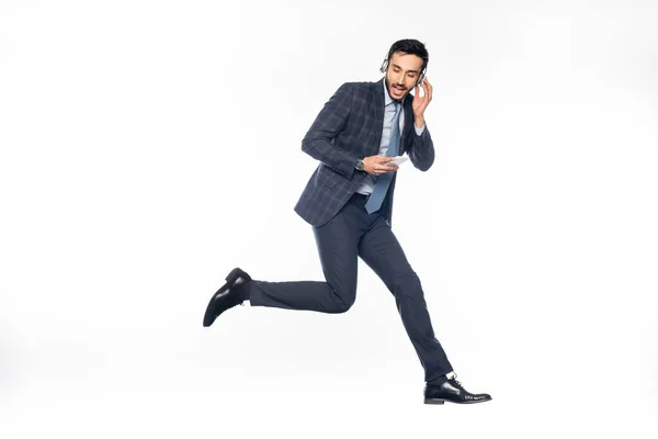 Hombre de negocios en traje saltando mientras escucha música en auriculares inalámbricos en blanco - foto de stock