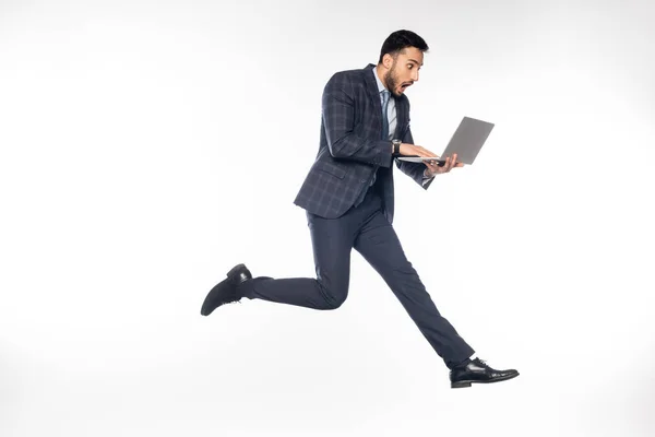 Sorprendido hombre de negocios en traje saltando mientras se utiliza el ordenador portátil en blanco - foto de stock