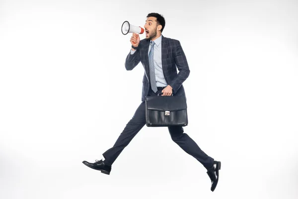 Hombre de negocios en traje saltando con maletín y gritando en altavoz en blanco - foto de stock