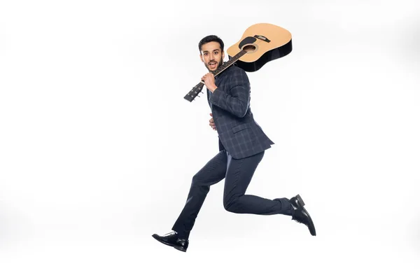 Homme d'affaires heureux en combinaison sautant avec guitare acoustique sur blanc — Photo de stock