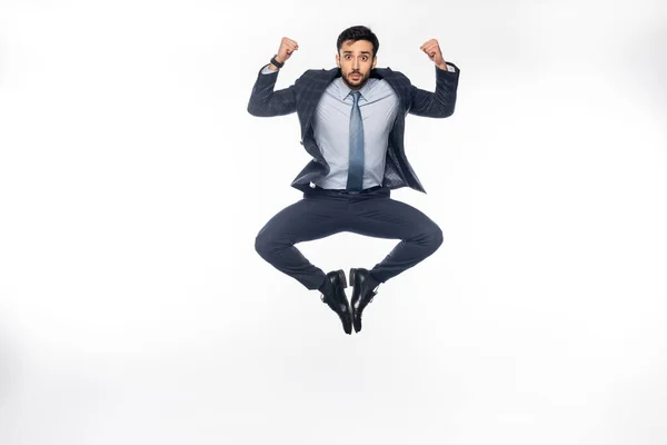 Businessman in suit jumping while showing muscles on white — Stock Photo
