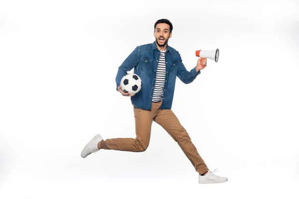 Homme heureux lévitant tout en tenant ballon de football et haut-parleur sur blanc — Photo de stock