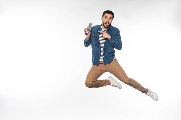 Happy man levitating while pointing at remote controller on white — Stock Photo