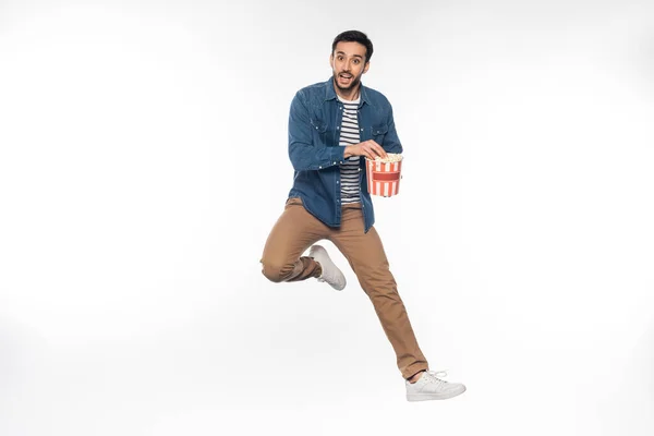 Glücklicher Mann schwebt, während er Popcorn-Eimer auf weiß hält — Stockfoto