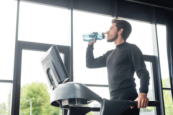 Vue latérale de l'homme eau potable sur tapis roulant dans le centre sportif — Photo de stock