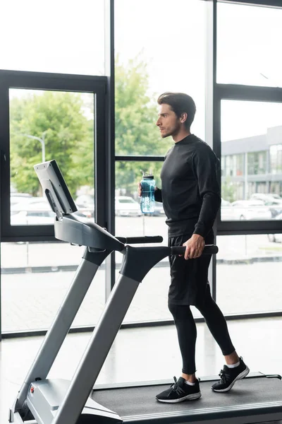 Side view of man holding sports bottle while running on treadmill in gym — Foto stock