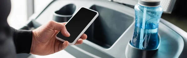 Cropped view of sportsman holding smartphone with blank screen near treadmill, banner — Stock Photo