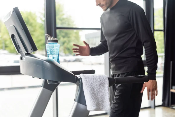 Vista ritagliata dell'allenamento sportivo sul tapis roulant vicino all'asciugamano e alla bottiglia sportiva in palestra — Foto stock