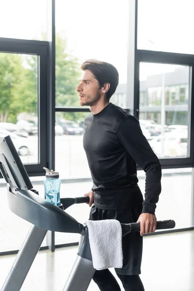 Sportler läuft auf Laufband neben Sportflasche und Handtuch im Fitnessstudio — Stockfoto
