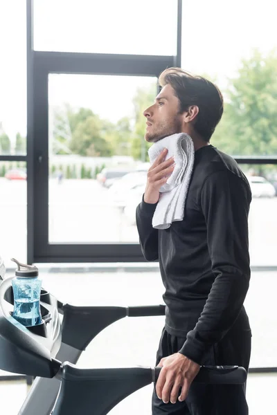 Vue latérale de la sportive tenant une serviette pendant l'entraînement sur tapis roulant dans la salle de gym — Photo de stock