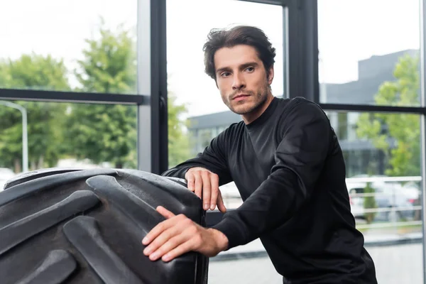 Sportsman standing near tire in sports center — Stock Photo