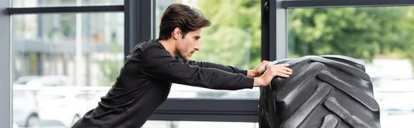 Vista lateral del deportista haciendo ejercicio con neumático en el gimnasio, pancarta - foto de stock