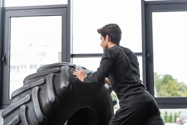 Brünette Mann in Sportbekleidung trainiert mit Reifen im Fitnessstudio — Stockfoto