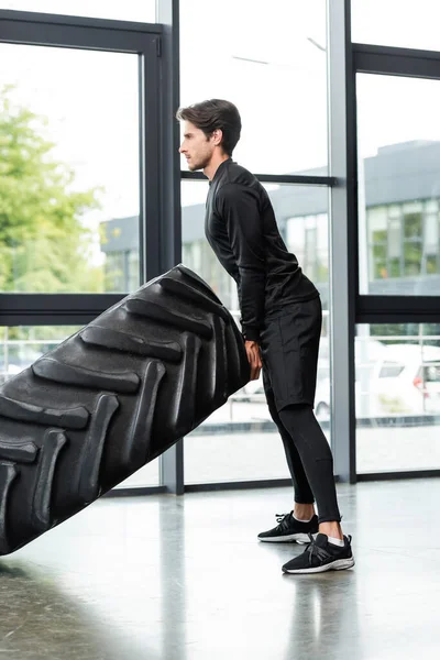 Side view of sportswoman training while lifting tire in sports center — Stock Photo