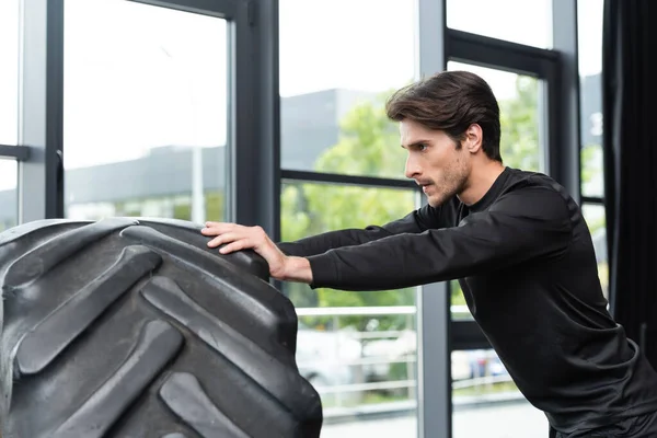 Brunette sportsman pushing tire during cross training in sports center — Stockfoto