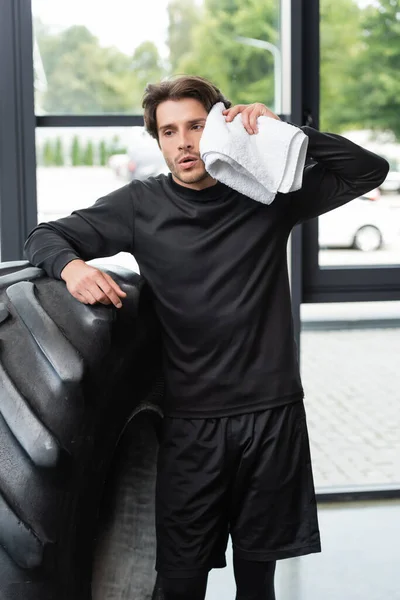 Tired sportsman wiping face with towel near tire in gym — Stock Photo