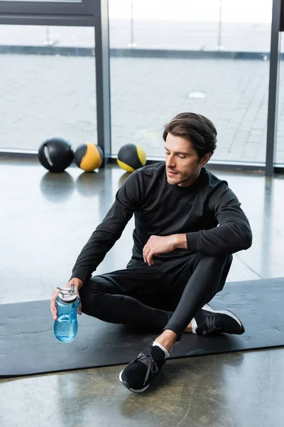 Deportista sosteniendo la botella de deporte en la alfombra de fitness en el centro deportivo - foto de stock