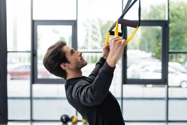 Side view of sportsman training with suspension straps in gym — Foto stock