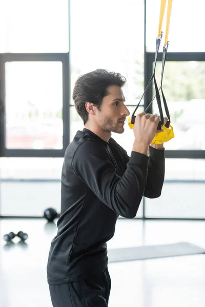 Side view of brunette sportswoman training with suspension straps in sports center — Stock Photo