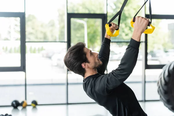 Side view of man in sportswear training with suspension straps in gym — Foto stock