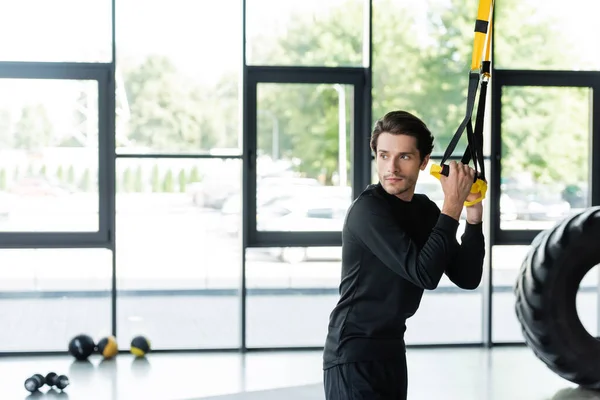 Спортсмен тренируется с подвесными ремнями и смотрит в тренажерный зал — стоковое фото