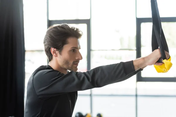 Vue latérale du sportif tenant des bretelles de suspension pendant l'entraînement en salle de gym — Photo de stock