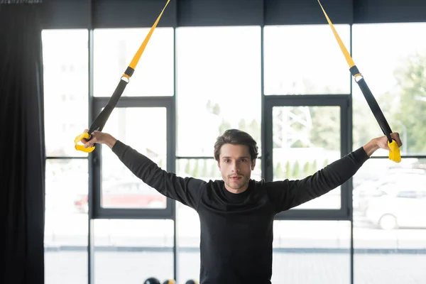 Sportsman looking at camera while training with suspension straps in sports center — Stock Photo