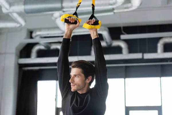 Sportsman working out with suspension straps in sports center — Stockfoto