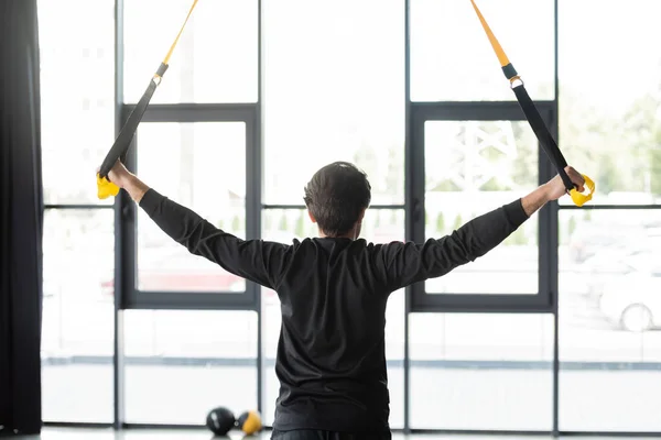 Back view of sportsman training with suspension straps in gym — Stock Photo