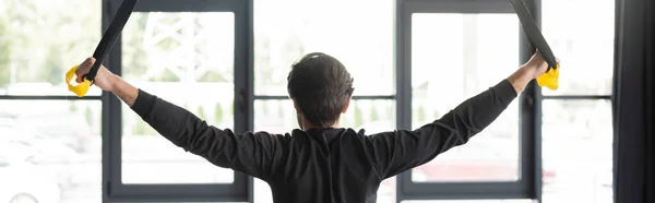 Vue arrière du sportif s'entraînant avec des sangles de suspension dans la salle de gym, bannière — Photo de stock