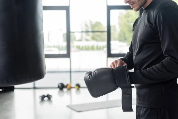 Vista ritagliata dello sportivo che indossa un guanto da boxe vicino al sacco da boxe in palestra — Foto stock