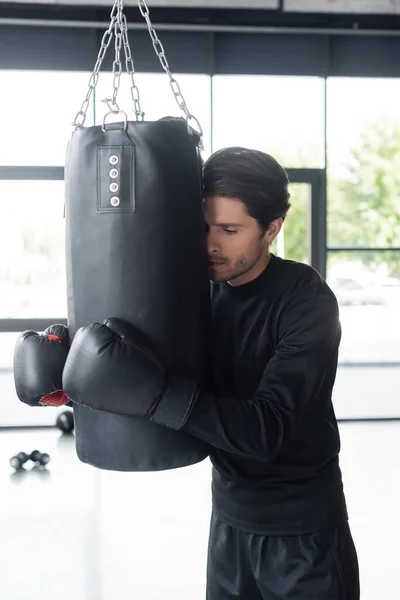 Sportler in Boxhandschuhen umarmt Boxsack im Fitnessstudio — Stockfoto