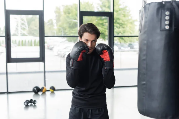 Sportsman in boxing gloves standing near punching bag while training in gym — Stock Photo