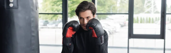 Brunette boxer in gloves standing near punching bag in gym, banner — Stock Photo