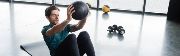 Brünetten Sportler beim Training mit Slam Ball in der Nähe von Kurzhanteln im Fitnessstudio, Banner — Stockfoto