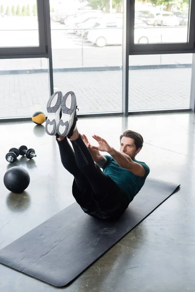 Brunette sportif travaillant sur tapis de fitness près de slam ball et haltères dans la salle de gym — Photo de stock