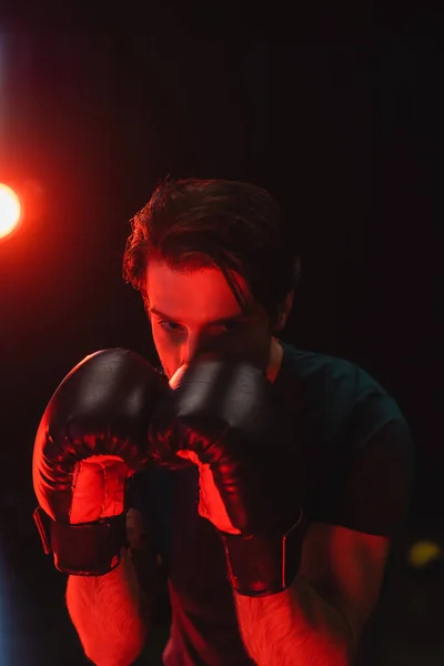 Sportsman in boxing gloves training on black background with red light — Stock Photo