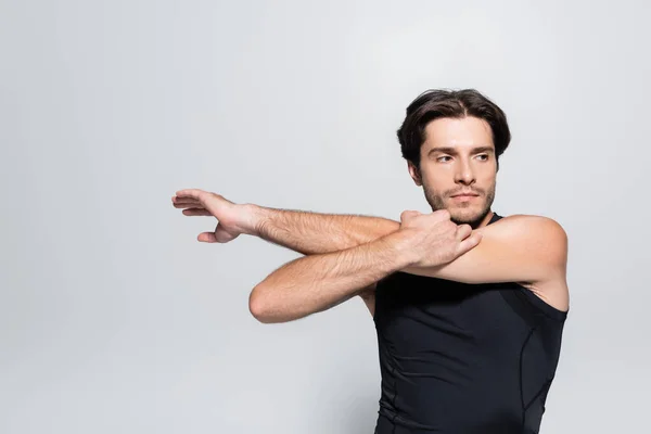 Brunette sportsman stretching arms isolated on grey — Stock Photo