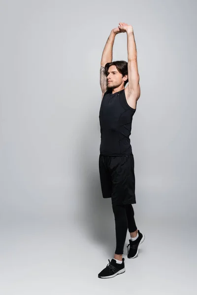 Full length of tattooed sportsman warming up on grey background — Stock Photo