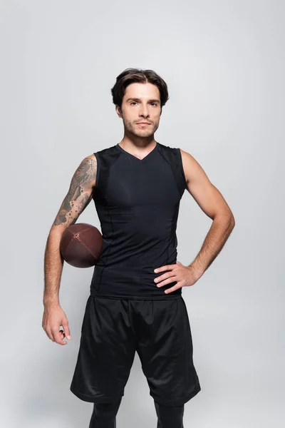 Татуйований спортсмен з м'ячем регбі дивиться на камеру ізольовано на сірому — стокове фото