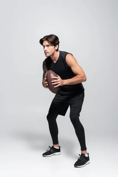 Full length of rugby player holding ball on grey background — Stock Photo