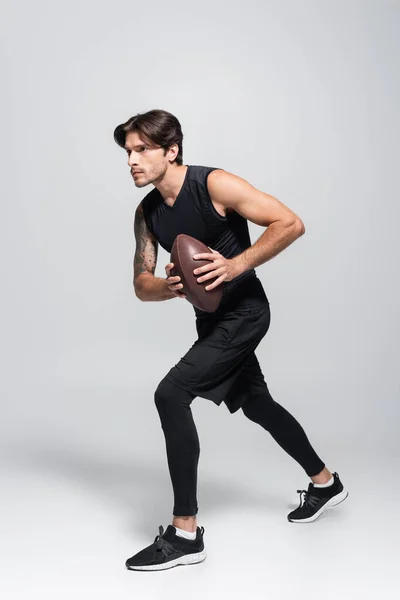 Jogador de rugby com bola correndo em fundo cinza — Fotografia de Stock